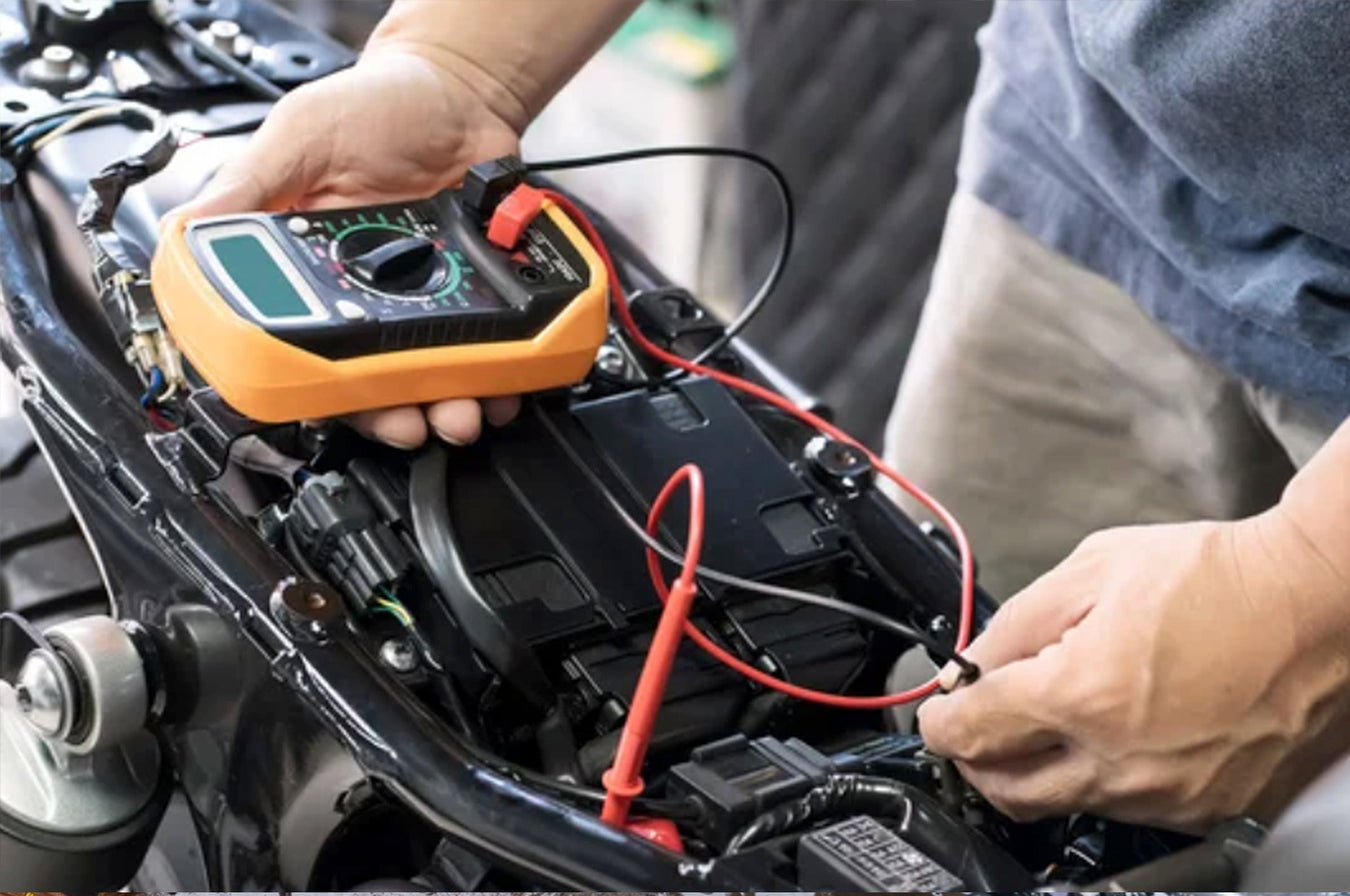 man standing over his v-twin motorcycle is seen testing its battery.